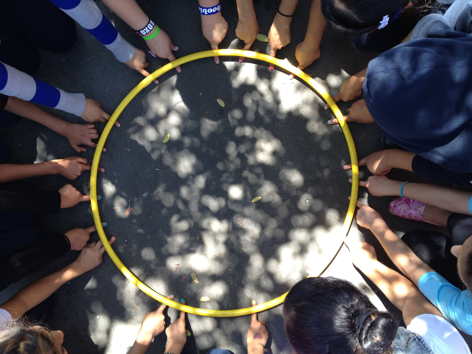 A circle of students' hands holding a yellow hula hoop from above.